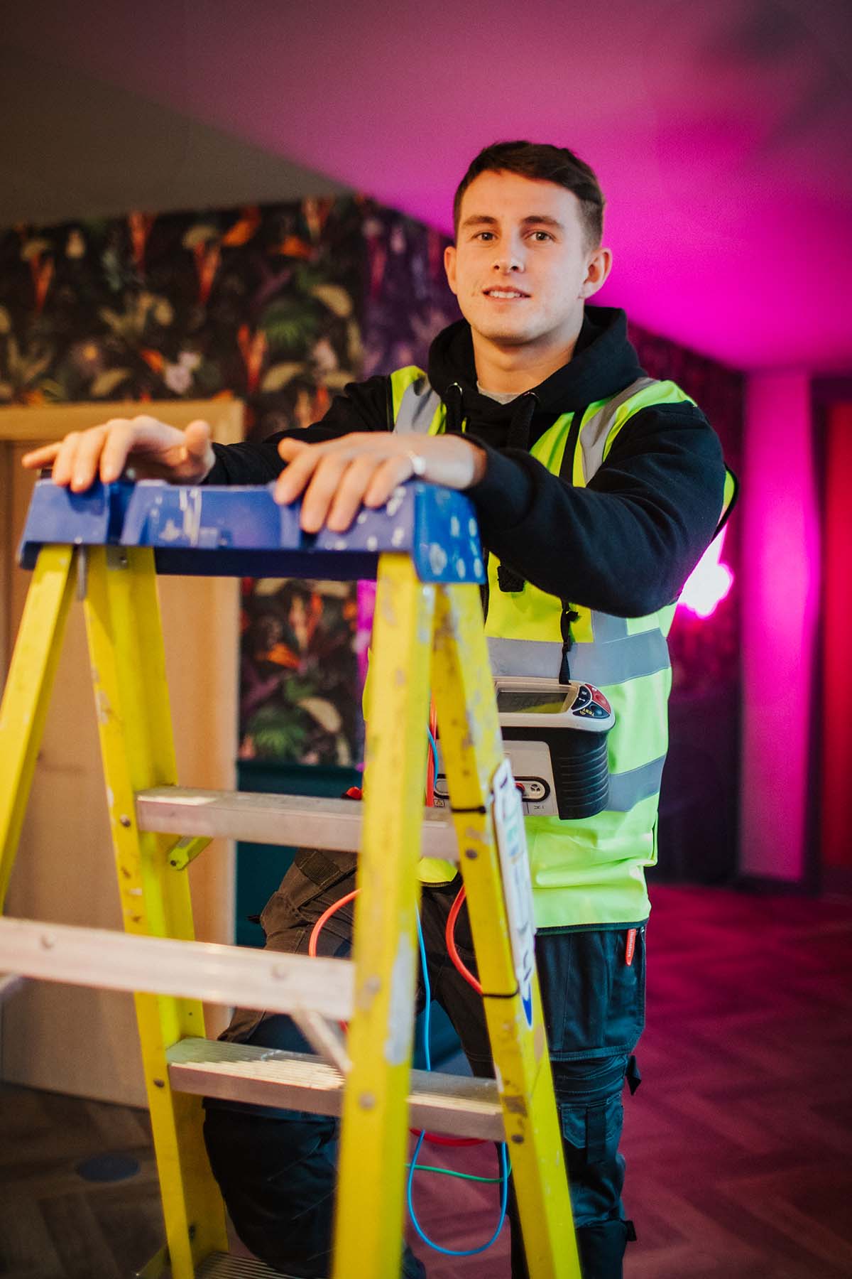 A person wearing a hi-vis whilst half climbing a ladder smiling towards the camera